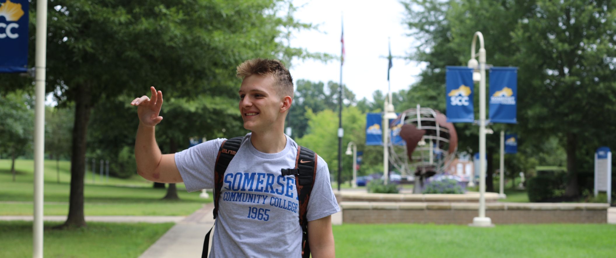 Male student walking on campus and waving