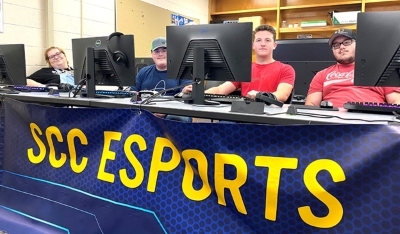 four students sitting at a table with computers and an SCC E-Sports banner