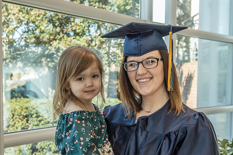 female graduate in cap and gown holding her little girl