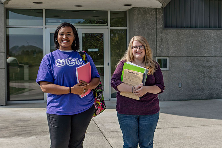 students holding their books outside smiling