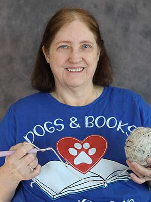Sandra Stevens holding a crochet hook and wearing a shirt that says 'Dogs & Books'