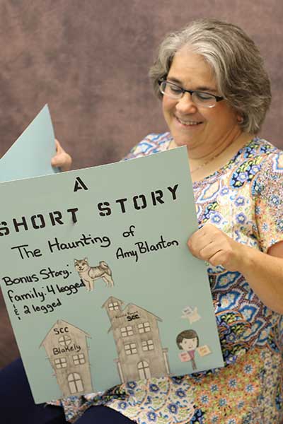 Amy Blanton reading a large storybook called 'The Haunting of Amy Blanton'