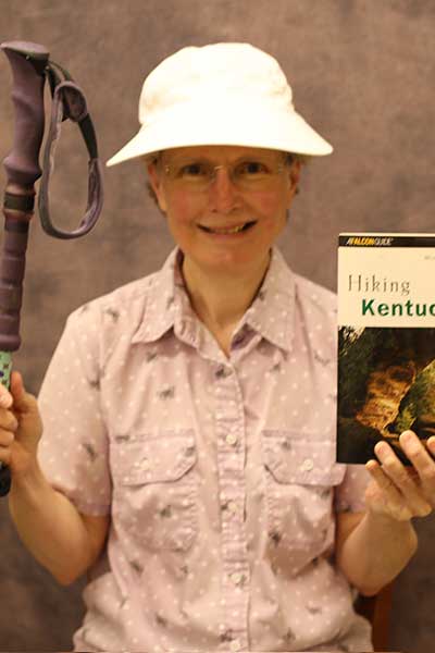 Cathy McFeeters holding a hiking stick in one hand and a 'Hiking Kentucky' book in the other hand