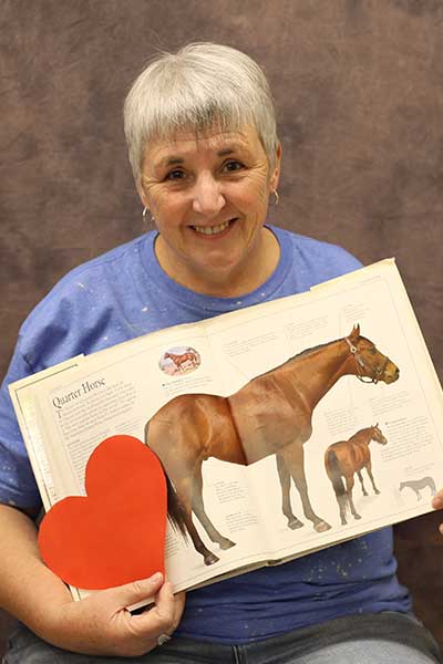 Rebecca Thurman holding a heart and a book open to a page about quarter horses