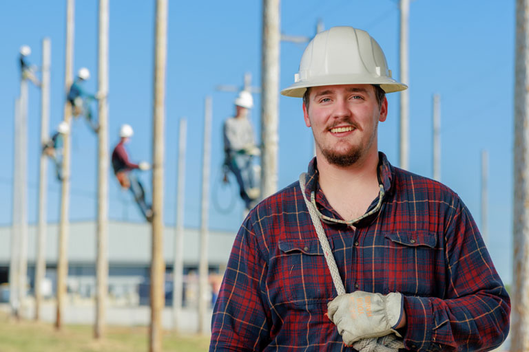 lineworkers standing in front of multiple other lineworkers and poles
