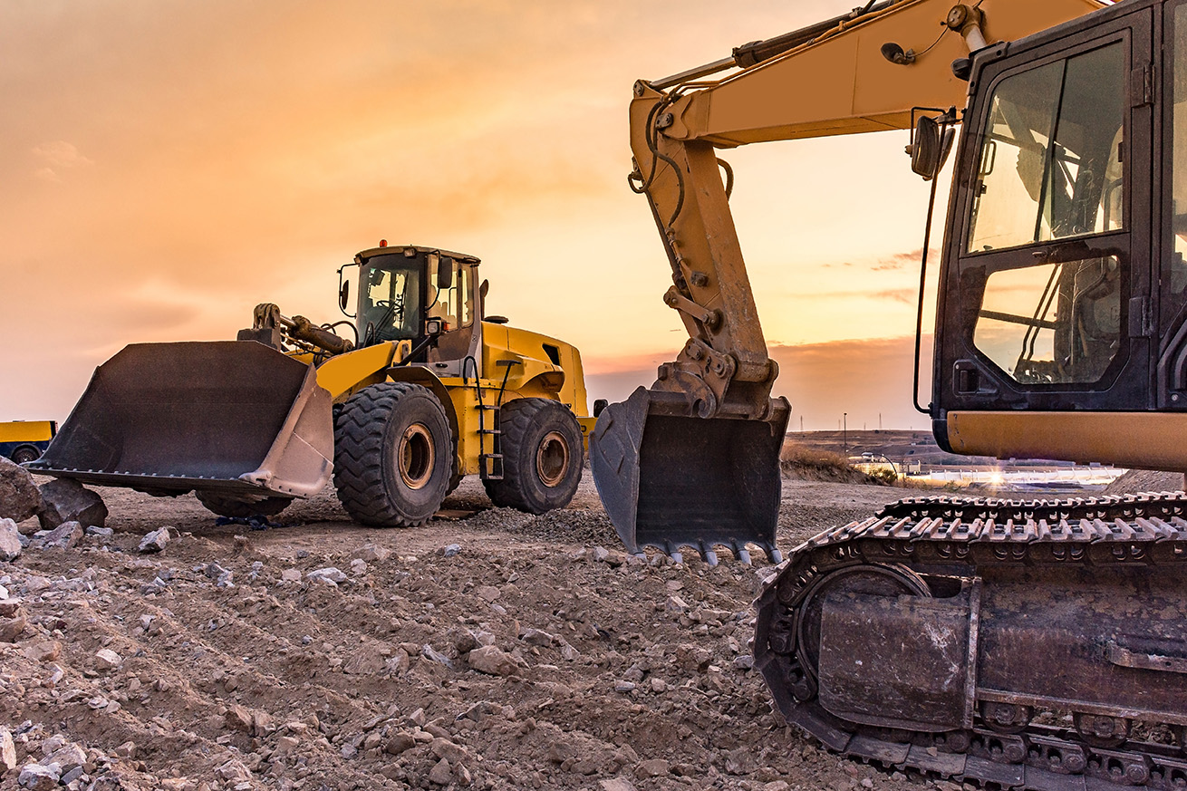 heavy equipment parked in front of a sunset 