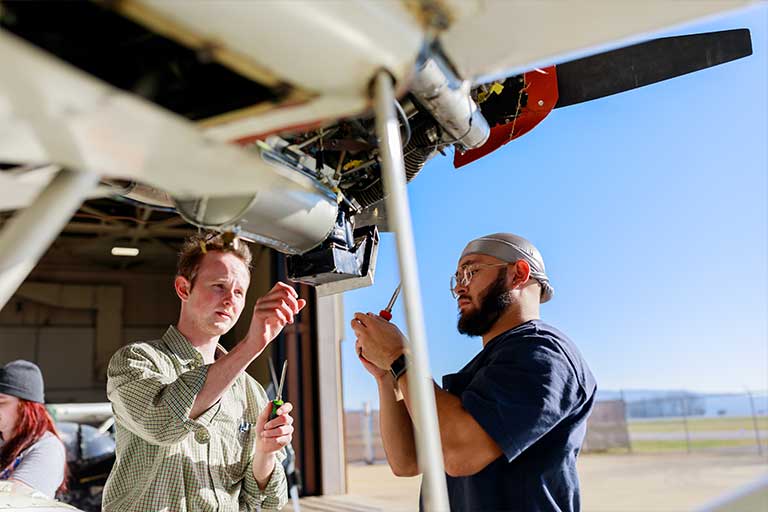 two students working on an airplane part