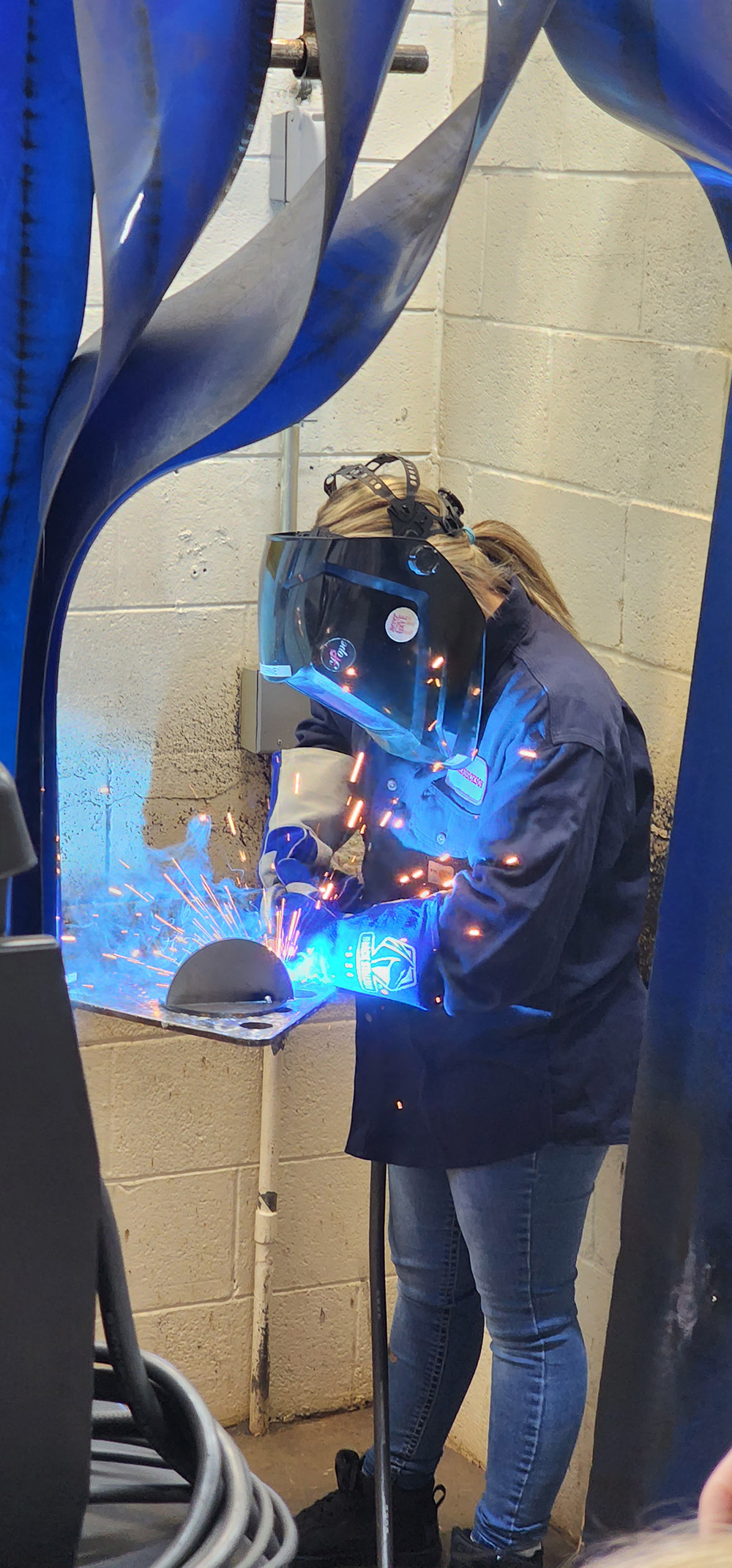 Student welding with the welding protection equipment while sparks and blue light shines.