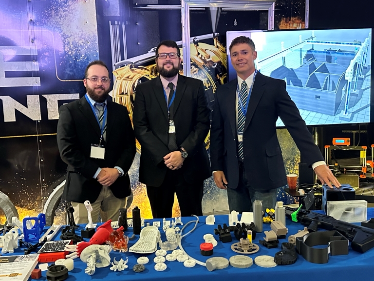 three men standing at table with 3d printed items at the SOAR Summit