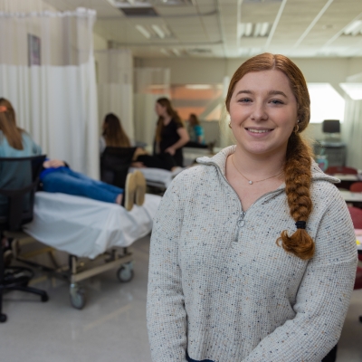 female students smiling with other students using sonography machines in a lab behind her