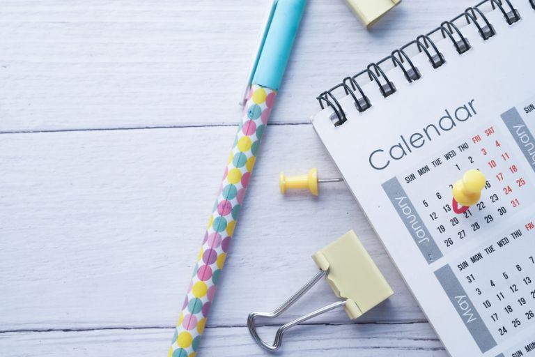 a calendar with yellow thumbtacks, a colorful pen, and a binder clip next to it